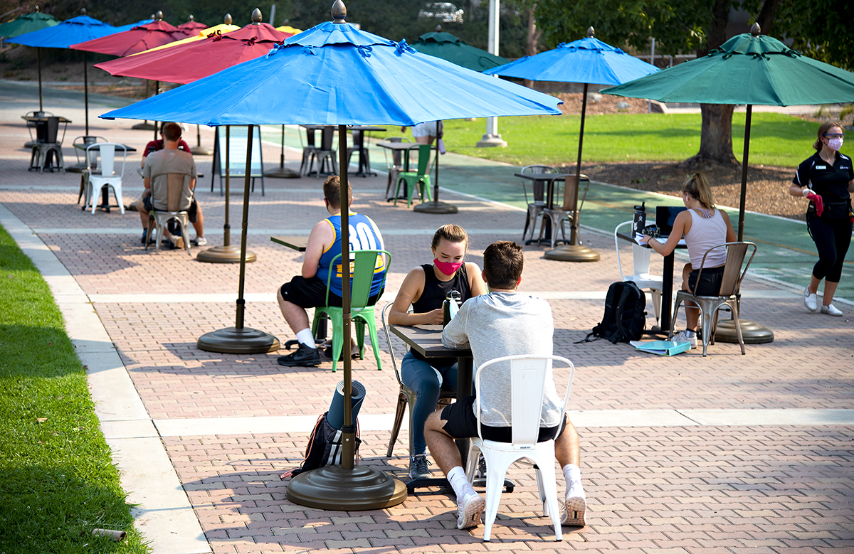 Students sitting at tables with umbrellas